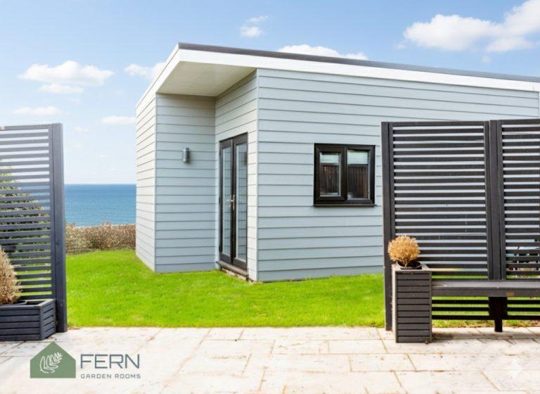 Garden room with dark-framed doors and windows, set in a garden with a panoramic sea view.